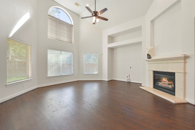 unfurnished living room with dark wood-type flooring, a high ceiling, a tiled fireplace, and plenty of natural light