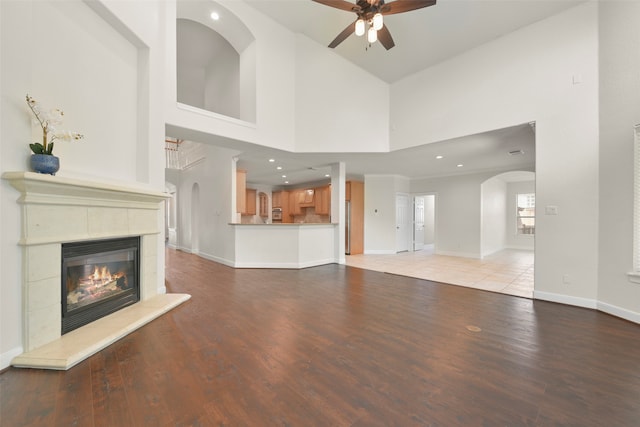 unfurnished living room featuring light wood-type flooring, a fireplace, ceiling fan, and a high ceiling