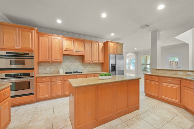 kitchen with ornamental molding, stainless steel appliances, light tile patterned flooring, and a center island