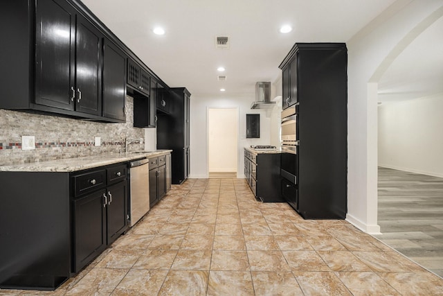 kitchen with sink, wall chimney exhaust hood, light stone countertops, appliances with stainless steel finishes, and tasteful backsplash