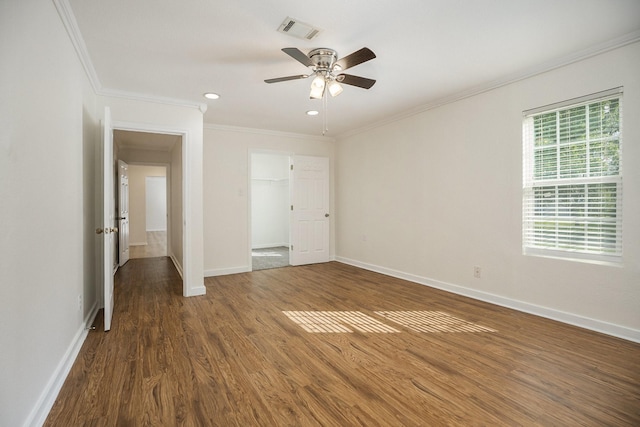 unfurnished bedroom featuring dark wood-type flooring, crown molding, ceiling fan, a spacious closet, and a closet