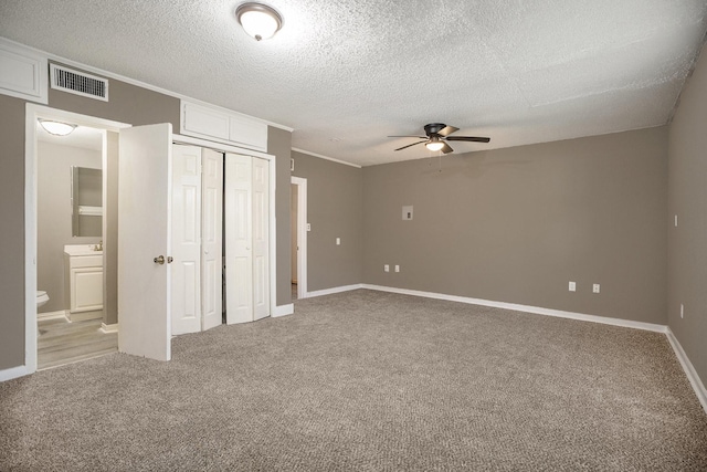 unfurnished bedroom featuring a textured ceiling, light colored carpet, ensuite bath, and ceiling fan