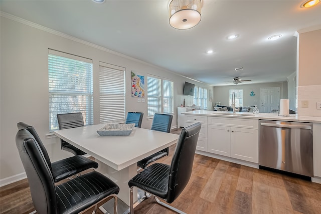 dining area featuring ornamental molding, a wealth of natural light, sink, and light hardwood / wood-style flooring