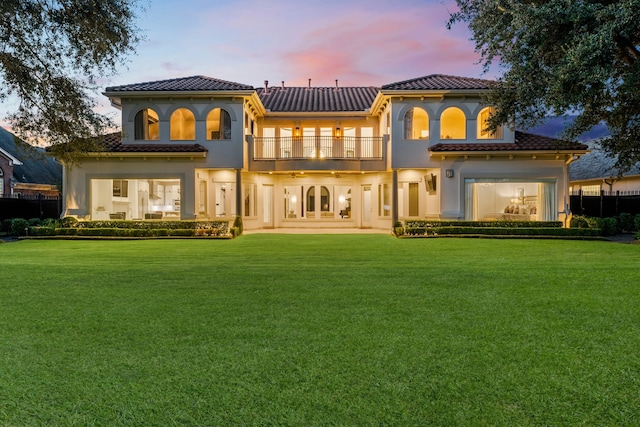 back house at dusk featuring a patio, a lawn, and a balcony