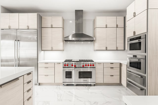 kitchen featuring high end appliances, light brown cabinets, and wall chimney range hood