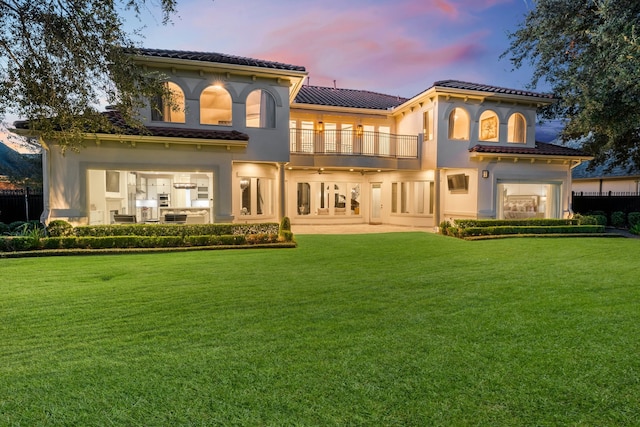 back house at dusk featuring a balcony, a patio, and a yard