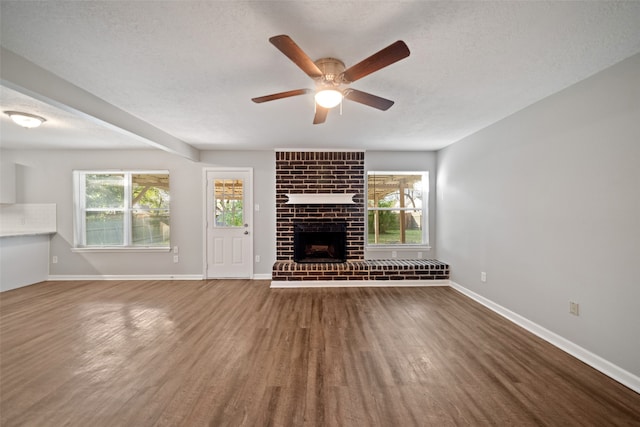 unfurnished living room with a brick fireplace, ceiling fan, a textured ceiling, and dark hardwood / wood-style flooring