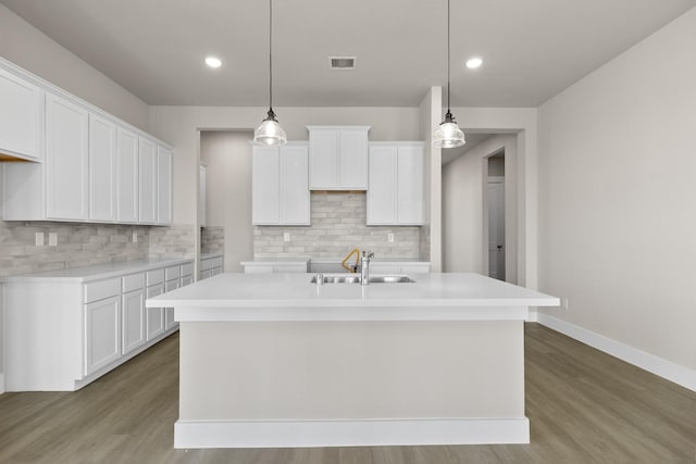 kitchen with decorative light fixtures, white cabinetry, and a kitchen island with sink