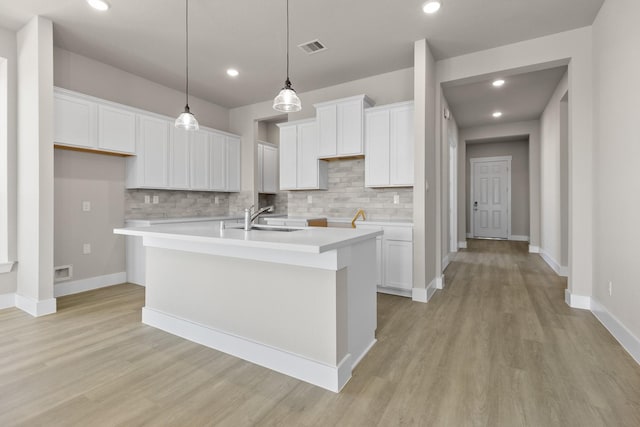 kitchen with light wood-type flooring, sink, a center island with sink, white cabinetry, and hanging light fixtures