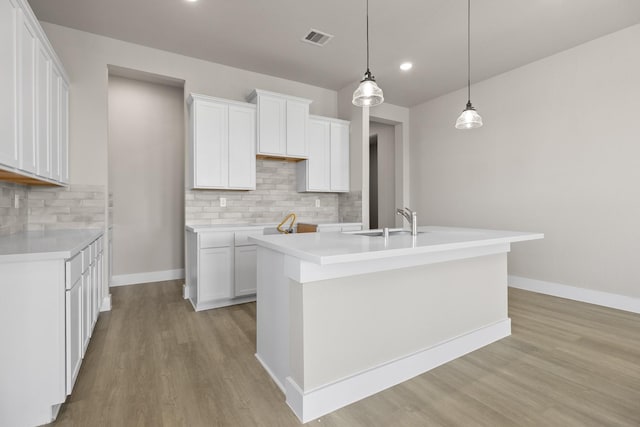 kitchen with backsplash, sink, decorative light fixtures, white cabinetry, and an island with sink