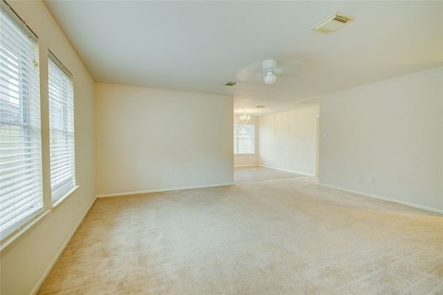 spare room featuring light carpet and ceiling fan with notable chandelier