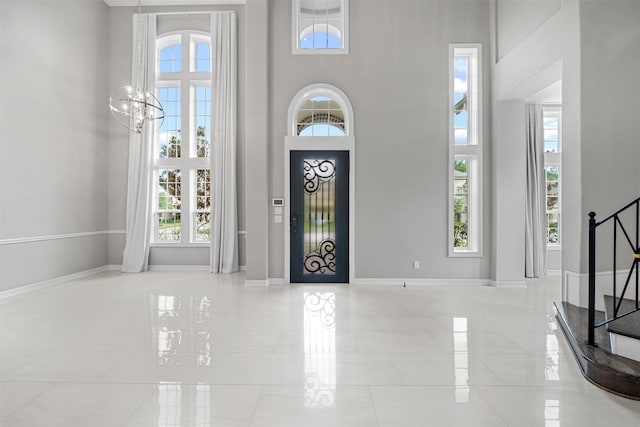 tiled entrance foyer featuring a high ceiling, plenty of natural light, and a notable chandelier