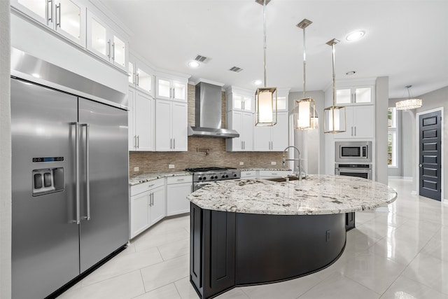 kitchen featuring built in appliances, sink, a kitchen island with sink, white cabinets, and wall chimney range hood