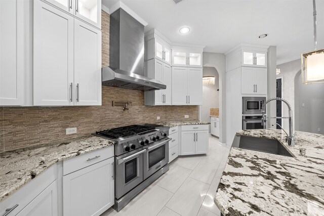 kitchen with decorative backsplash, sink, wall chimney range hood, white cabinetry, and appliances with stainless steel finishes