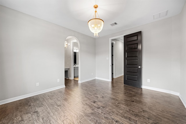 spare room with dark wood-type flooring and a notable chandelier