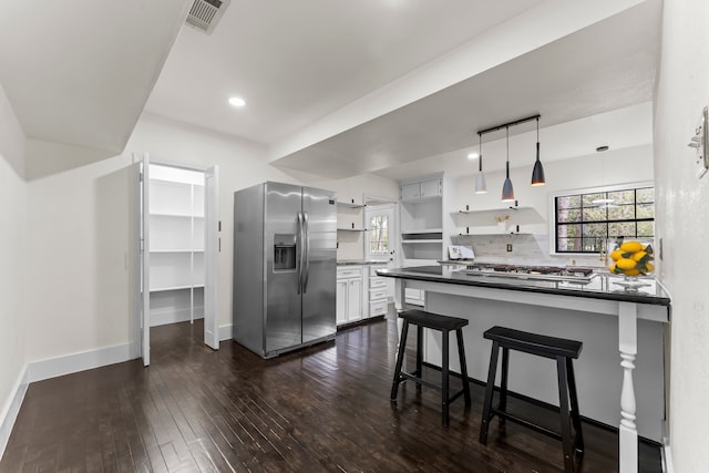 kitchen featuring stainless steel appliances, decorative light fixtures, a kitchen bar, white cabinets, and dark wood-type flooring