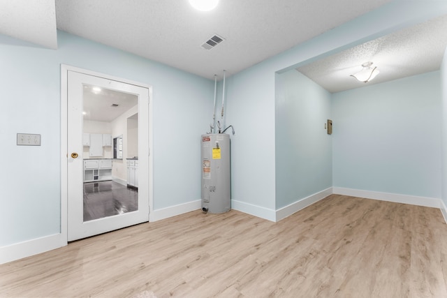 basement featuring electric water heater, light hardwood / wood-style flooring, and a textured ceiling