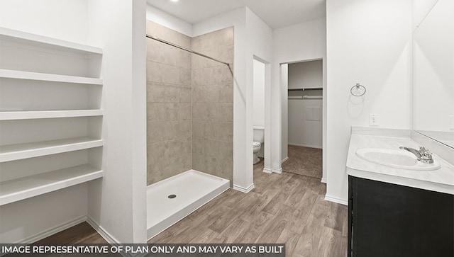 bathroom with toilet, vanity, hardwood / wood-style flooring, and tiled shower