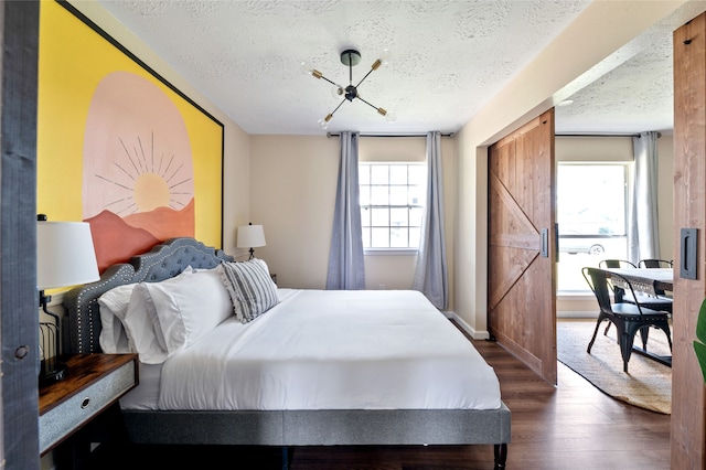 bedroom with a textured ceiling, a barn door, multiple windows, and dark hardwood / wood-style floors