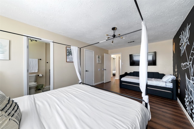 bedroom featuring ensuite bathroom, dark wood-type flooring, a textured ceiling, and a chandelier