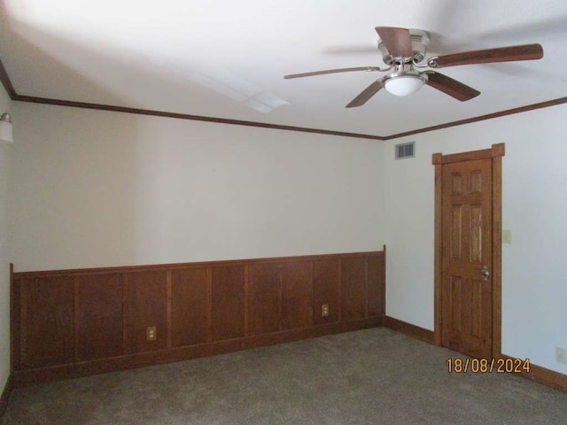 empty room with wood walls, carpet flooring, ceiling fan, and crown molding