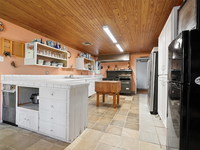 kitchen featuring black fridge, stainless steel fridge, tile counters, white cabinetry, and wood ceiling