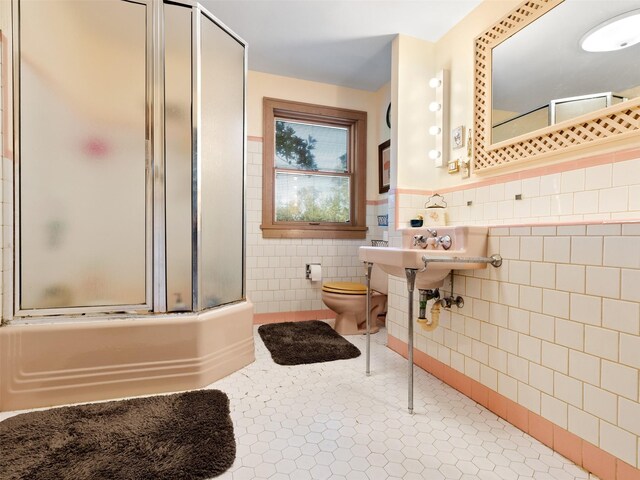 bathroom with tile patterned floors, enclosed tub / shower combo, tile walls, and toilet