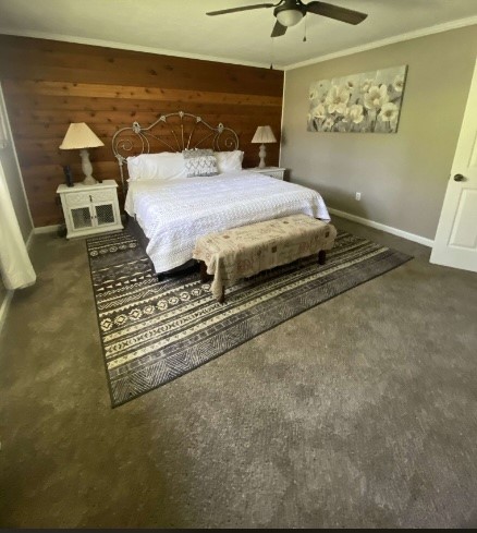 bedroom featuring ornamental molding, wooden walls, dark carpet, and ceiling fan