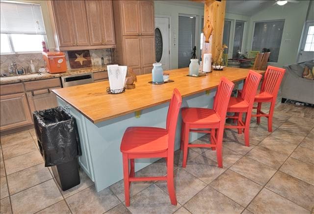 kitchen featuring tasteful backsplash, wooden counters, light tile patterned floors, a breakfast bar area, and a center island