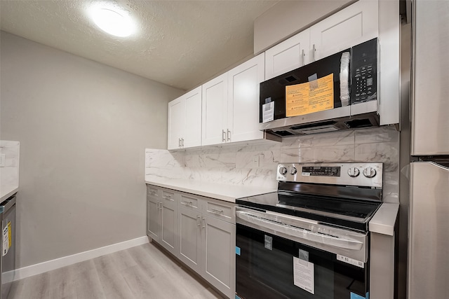 kitchen featuring stainless steel appliances, white cabinets, light wood-type flooring, and tasteful backsplash