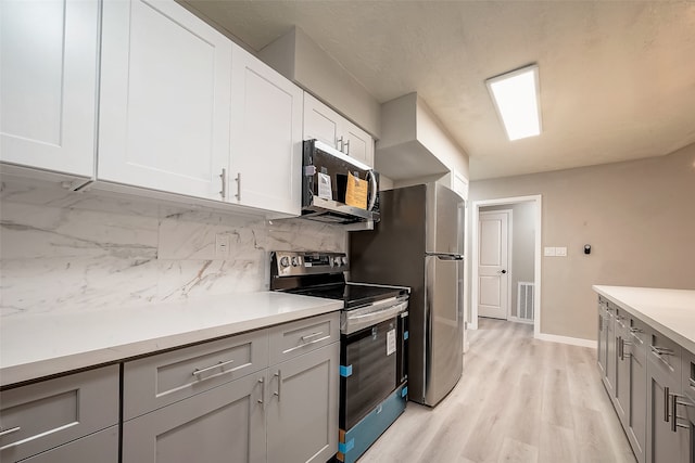 kitchen with tasteful backsplash, stainless steel appliances, white cabinetry, gray cabinets, and light hardwood / wood-style flooring