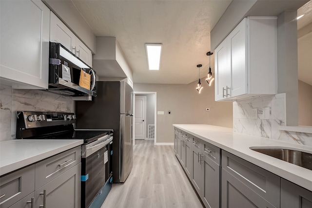 kitchen featuring white cabinets, decorative backsplash, hanging light fixtures, light wood-type flooring, and appliances with stainless steel finishes