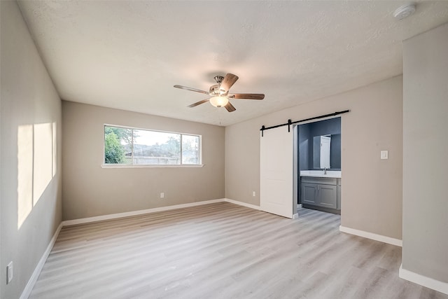 empty room with a textured ceiling, a barn door, sink, ceiling fan, and light wood-type flooring