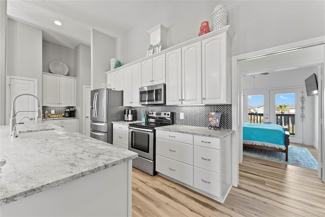 kitchen with stainless steel appliances, white cabinetry, sink, backsplash, and light hardwood / wood-style flooring