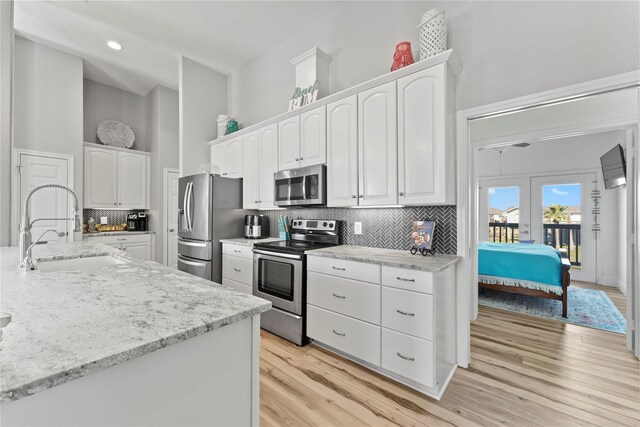 2423 Sandpiper, Crystal Beach, TX 77650 - kitchen with appliances with stainless steel finishes, a sink, white cabinetry, decorative backsplash, and light wood finished floors