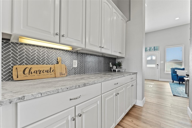 2423 Sandpiper, Crystal Beach, TX 77650 - kitchen featuring backsplash, white cabinetry, baseboards, light wood-style floors, and light stone counters
