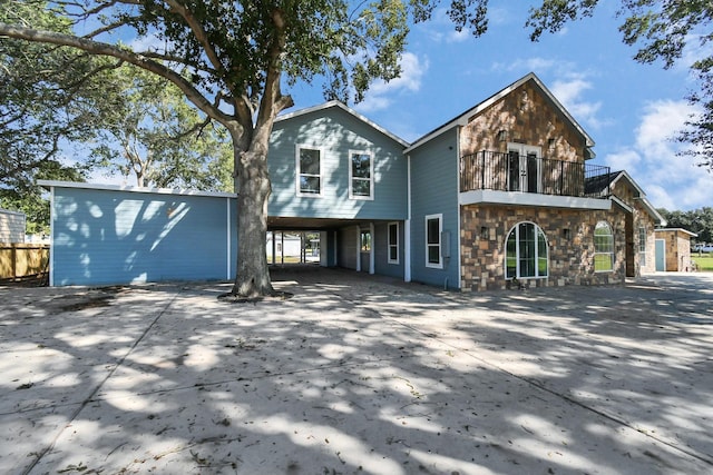 view of front facade featuring a balcony, stone siding, driveway, and a carport