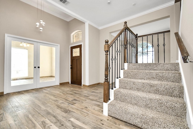 foyer featuring an inviting chandelier, french doors, ornamental molding, a towering ceiling, and wood-type flooring