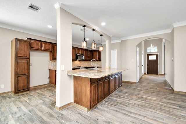 kitchen featuring light stone countertops, pendant lighting, light hardwood / wood-style floors, decorative backsplash, and ornamental molding