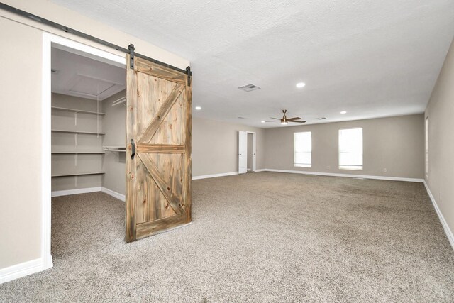 interior space with a barn door, ceiling fan, and a textured ceiling