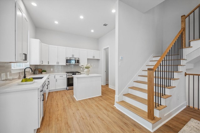 kitchen with stainless steel appliances, white cabinets, sink, a kitchen island, and light hardwood / wood-style flooring