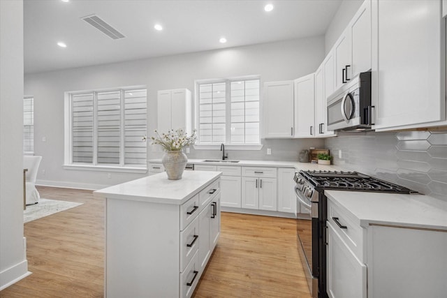 kitchen with light hardwood / wood-style floors, sink, a kitchen island, white cabinetry, and appliances with stainless steel finishes