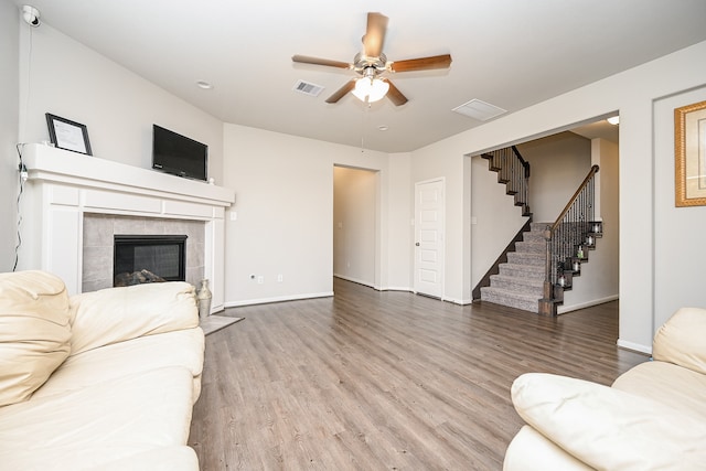 living room with ceiling fan, wood-type flooring, and a tiled fireplace