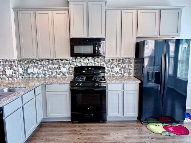 kitchen with black appliances, tasteful backsplash, light stone counters, and light hardwood / wood-style floors