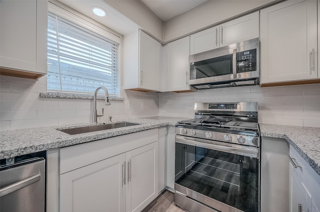 kitchen with light stone countertops, sink, stainless steel appliances, backsplash, and white cabinets