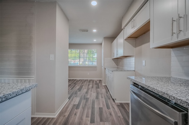 kitchen with light hardwood / wood-style flooring, stainless steel dishwasher, decorative backsplash, light stone countertops, and white cabinetry