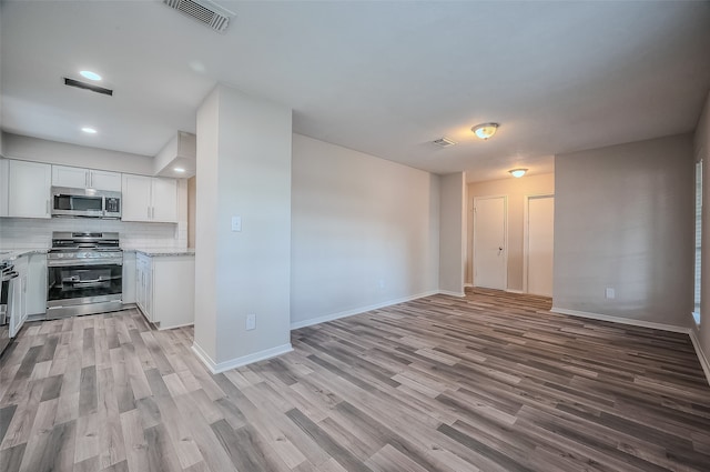 kitchen featuring white cabinetry, stainless steel appliances, light stone counters, decorative backsplash, and light wood-type flooring