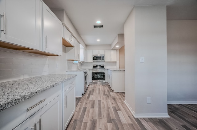 kitchen featuring decorative backsplash, light stone countertops, light wood-type flooring, stainless steel appliances, and white cabinets