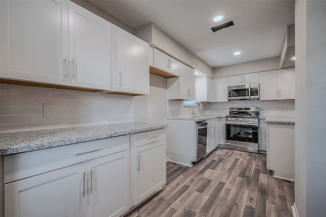 kitchen with white cabinetry, sink, light hardwood / wood-style floors, decorative backsplash, and appliances with stainless steel finishes