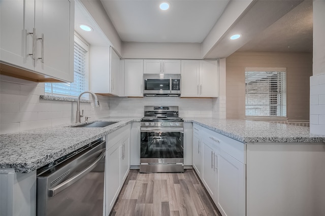 kitchen featuring kitchen peninsula, light stone countertops, stainless steel appliances, sink, and white cabinets